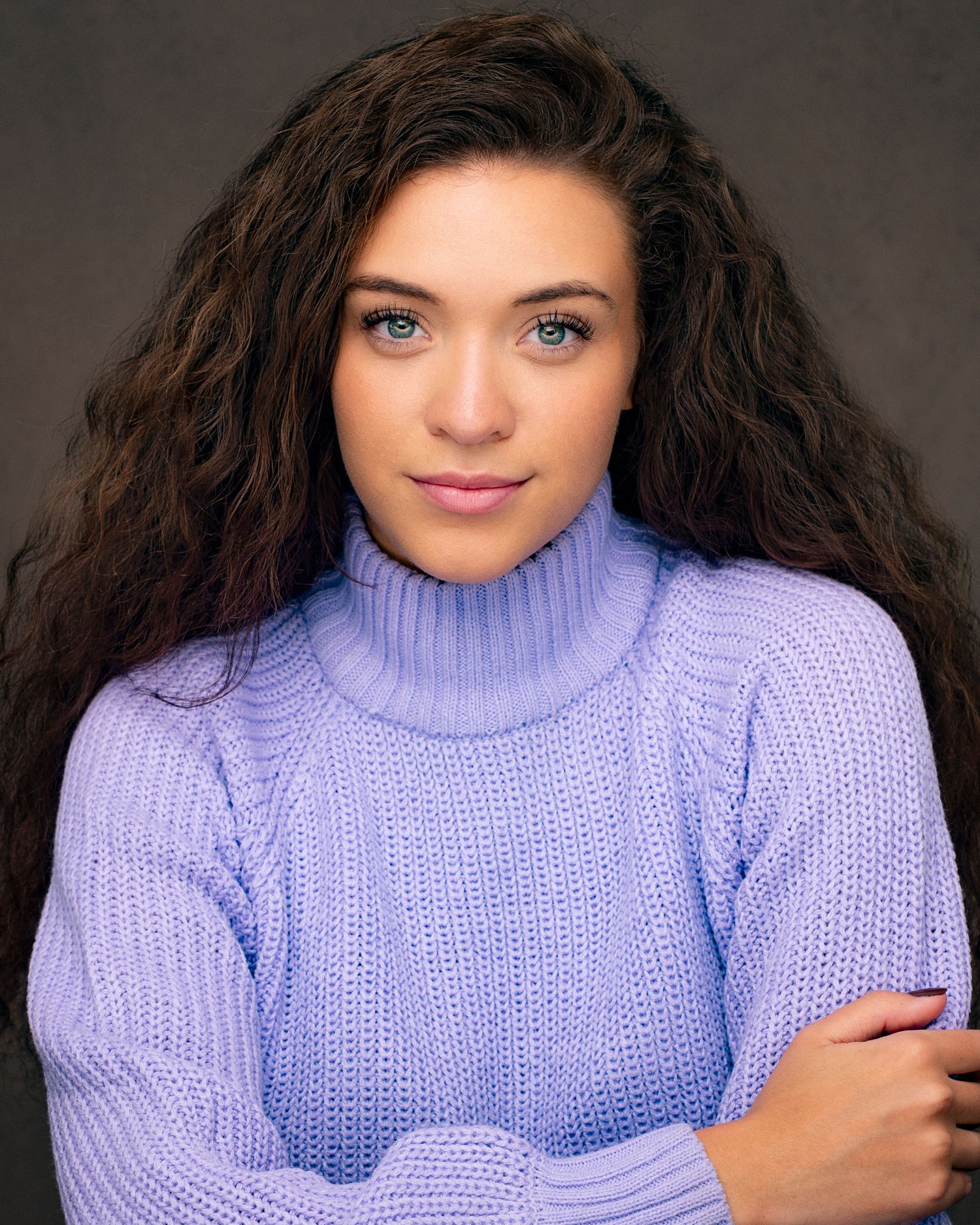 Portrait of a model in a lavender turtleneck sweater with dark curly hair.
