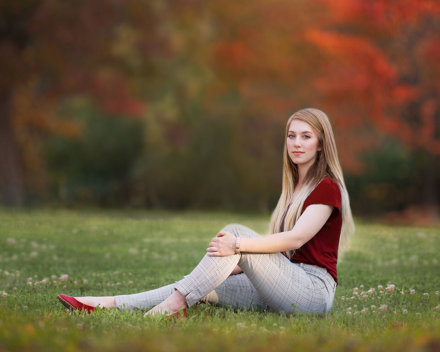 Beautiful blonde woman sits in the grass with fall foliage all around