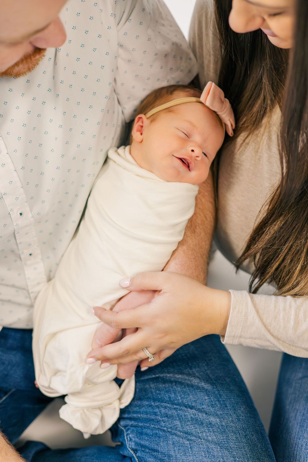 Parents tenderly holding sleeping newborn baby wrapped in white swaddle.
