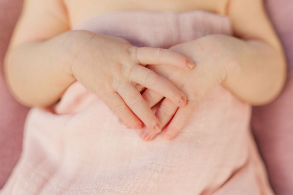 Close-up of tiny baby hands resting on soft pink fabric.