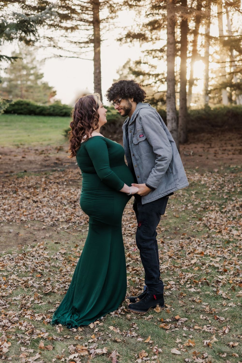 Romantic maternity photo of couple in forest setting during golden hour.