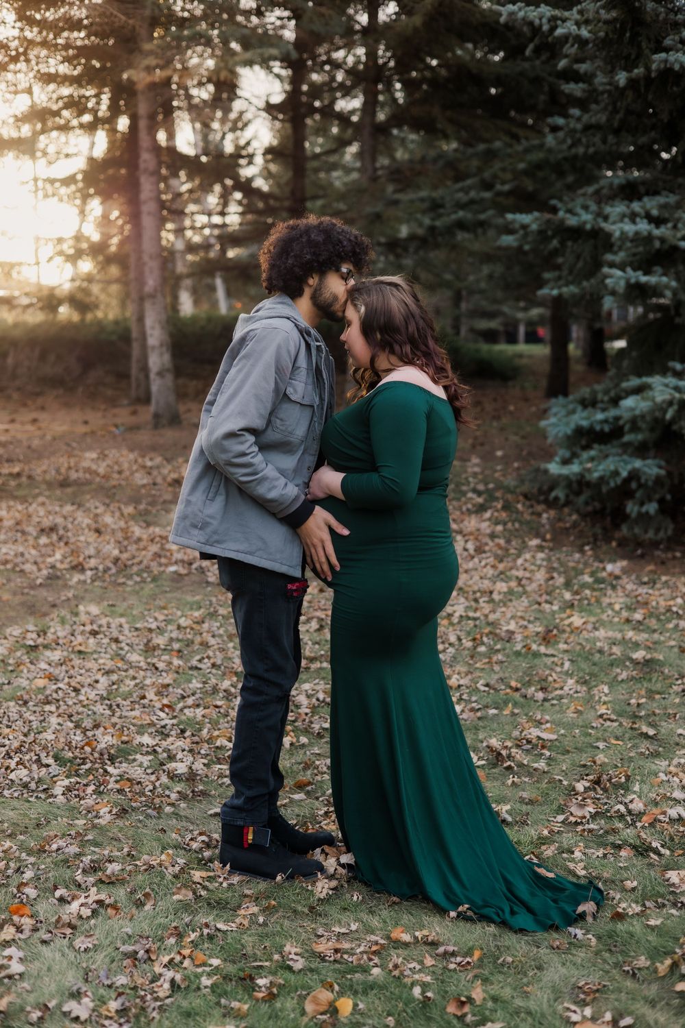 Intimate maternity portrait of couple embracing in forest setting at sunset.