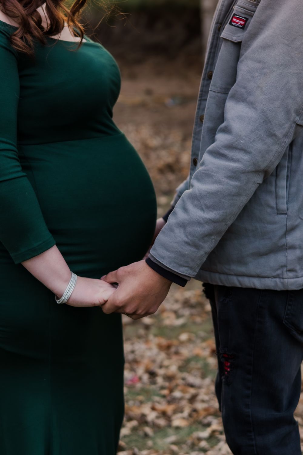 Close-up of expectant couple holding hands, woman wearing emerald green dress.