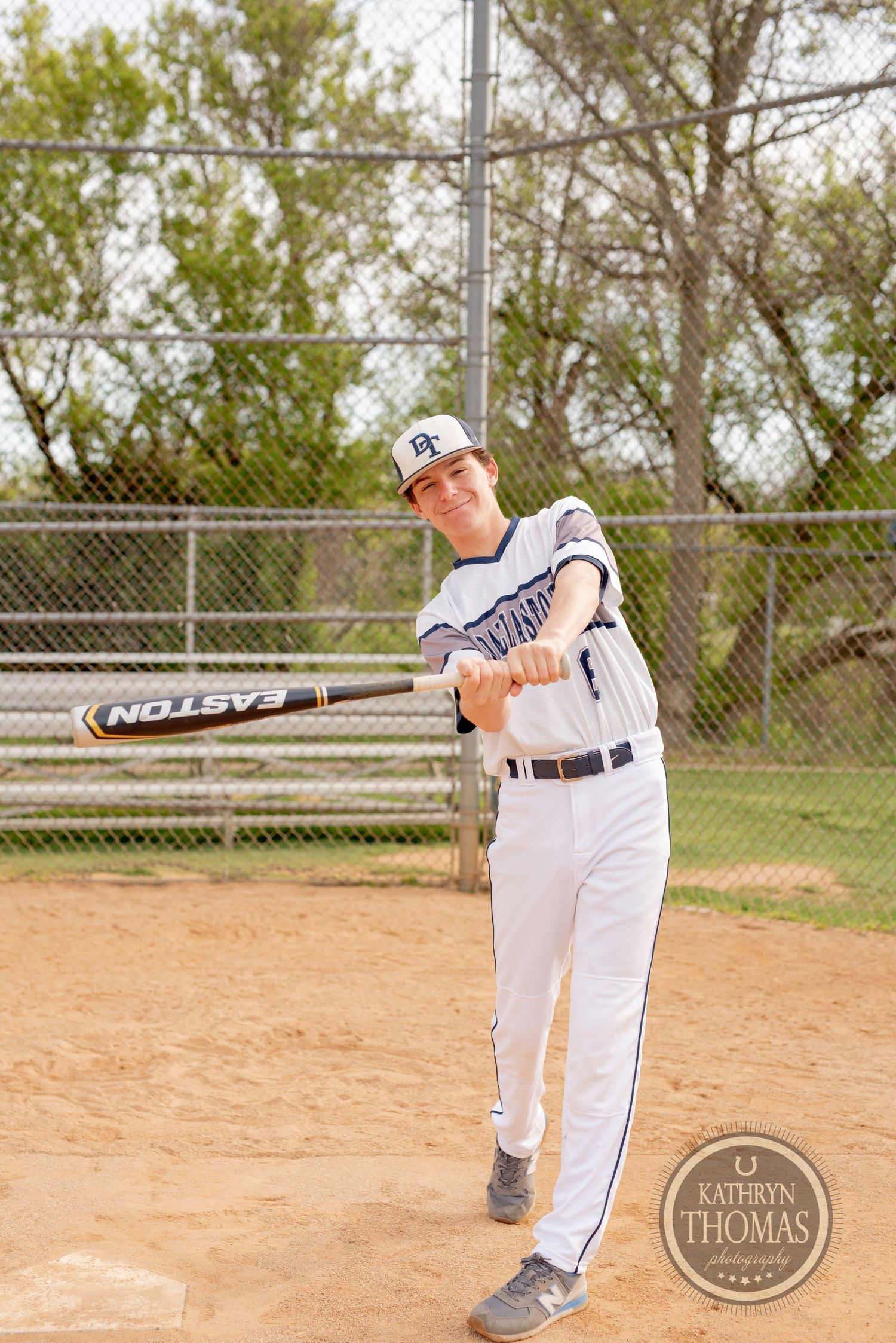 Baseball player in white uniform swings a bat during practice on dirt field.