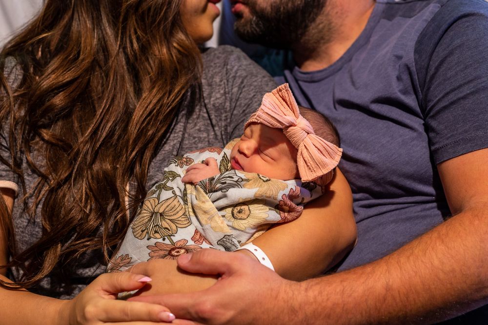 Close-up of newborn baby being cradled in floral outfit.