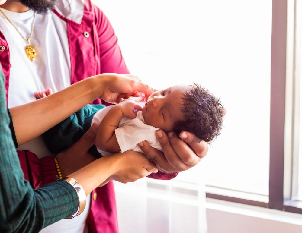 Caregivers tenderly hold and care for newborn baby near window.