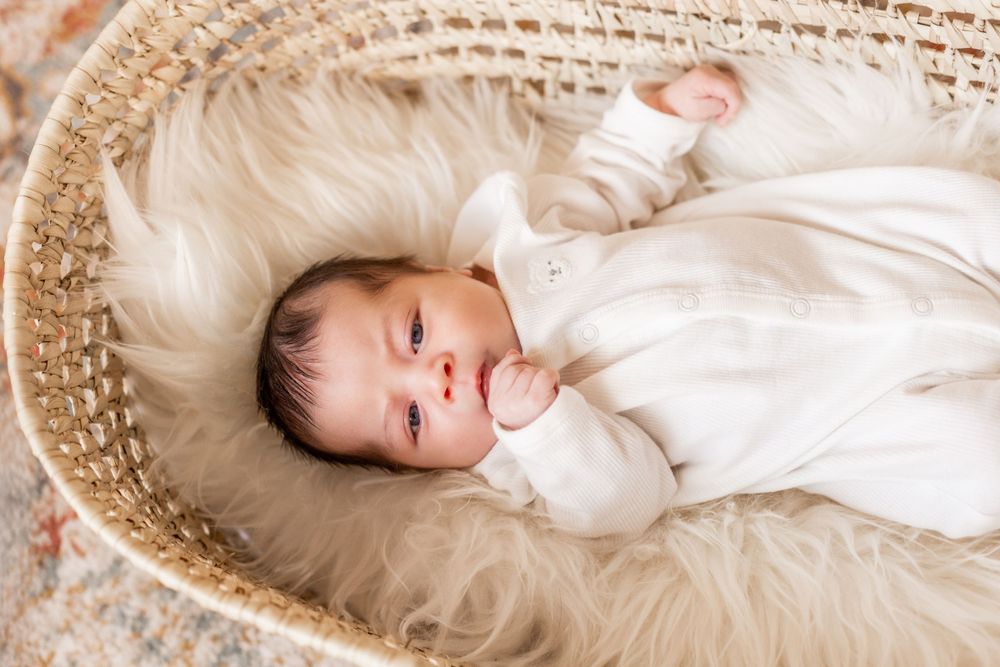 Smiling baby lying in woven basket on fluffy white blanket.