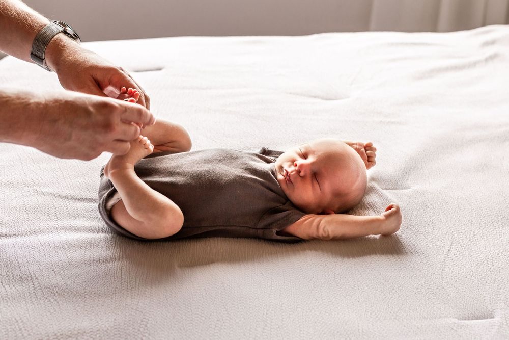 Gentle hands dress a sleeping newborn baby on white bedding.