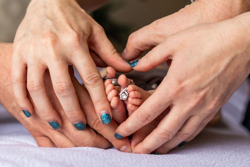 Close up of hands gently touching tiny newborn baby feet on white fabric.