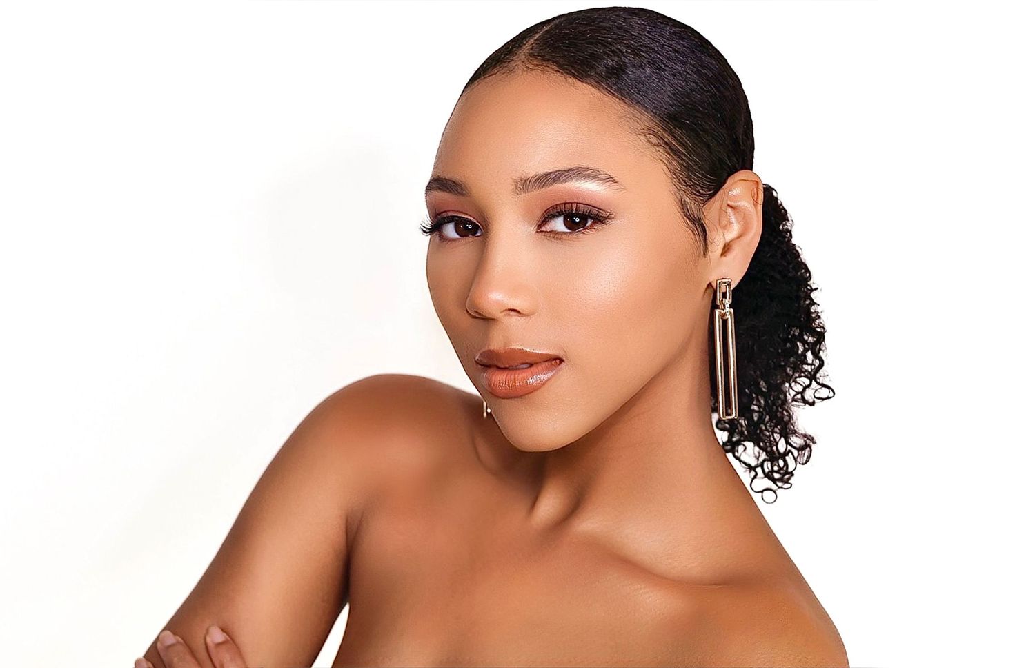 Glamorous portrait of a woman with dangling earrings and curly hair styled in a low updo.