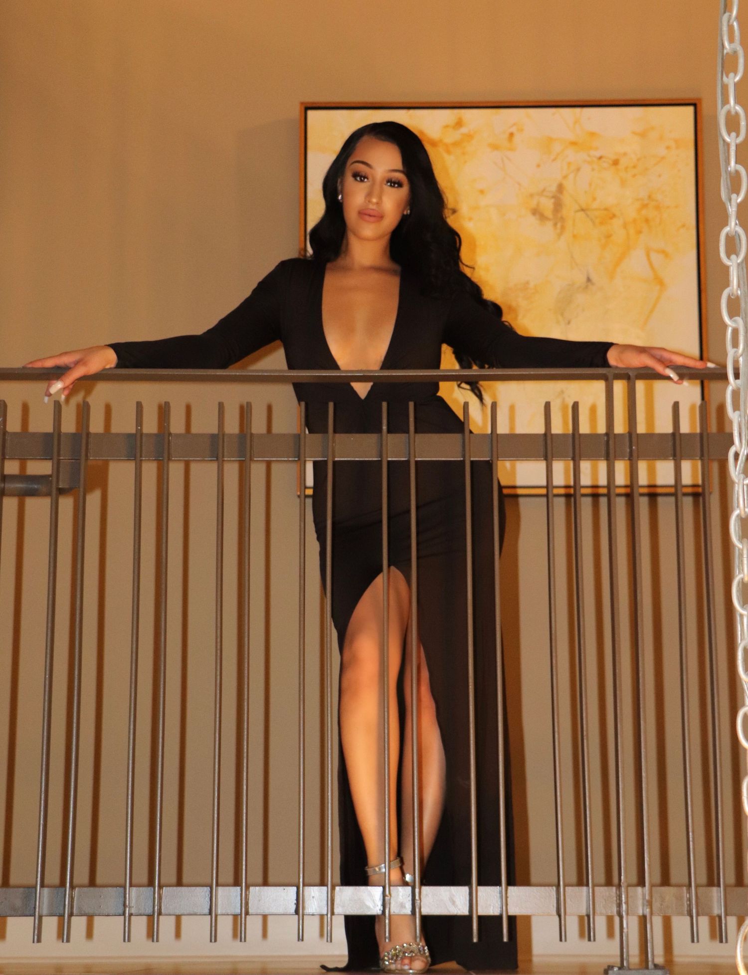 A woman in a black dress poses dramatically at a balcony railing.