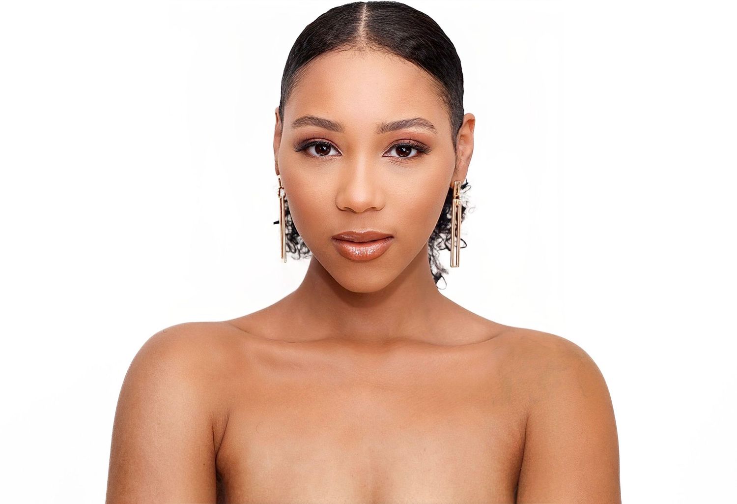 Close-up beauty portrait of a woman wearing natural makeup and sleek pulled back hair against white background.