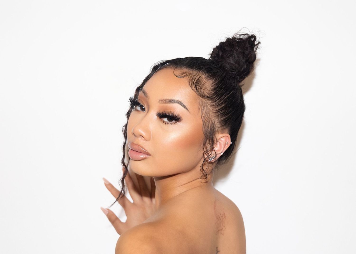 Studio beauty portrait with glowing makeup and hair in sleek top bun against white background.