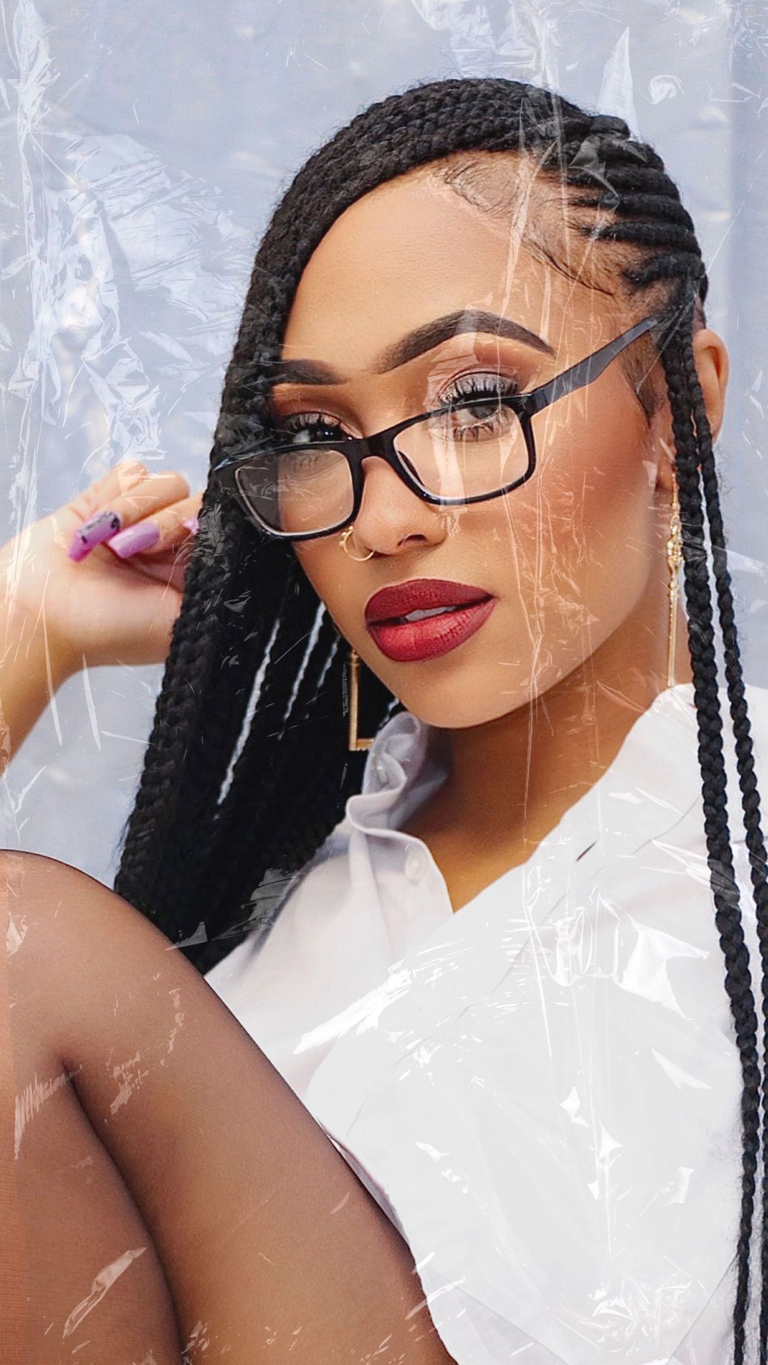 Portrait of a person wearing glasses with long braided hair and red lipstick against white backdrop.