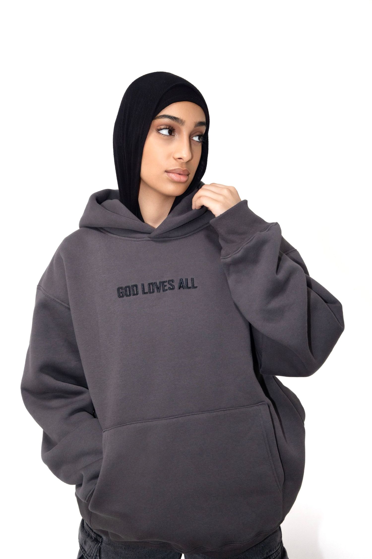 A gray oversized hoodie with 'GOD LOVES ALL' text embroidered on the front.