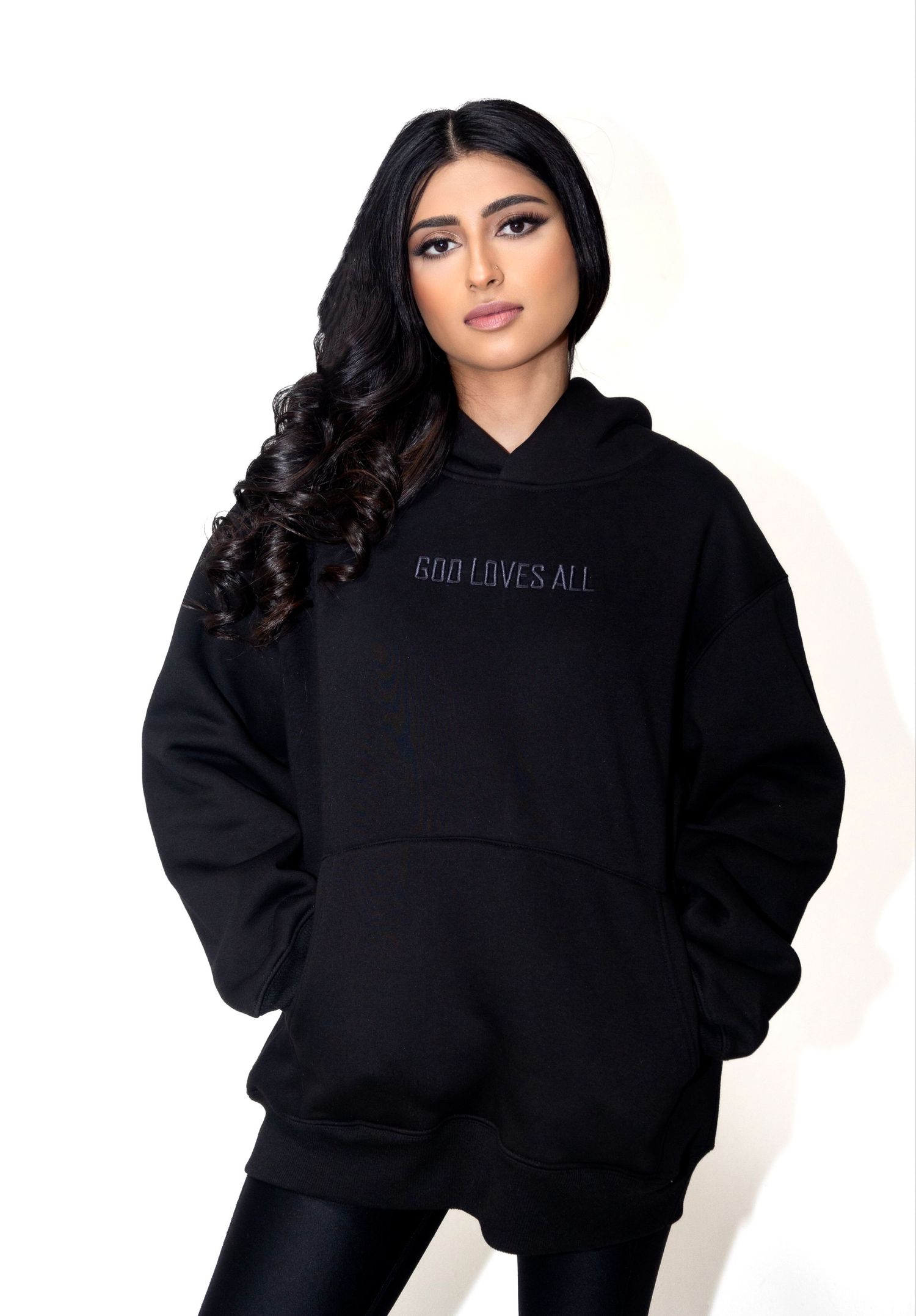A black oversized hoodie with 'GOD LOVES ALL' text against a white background.