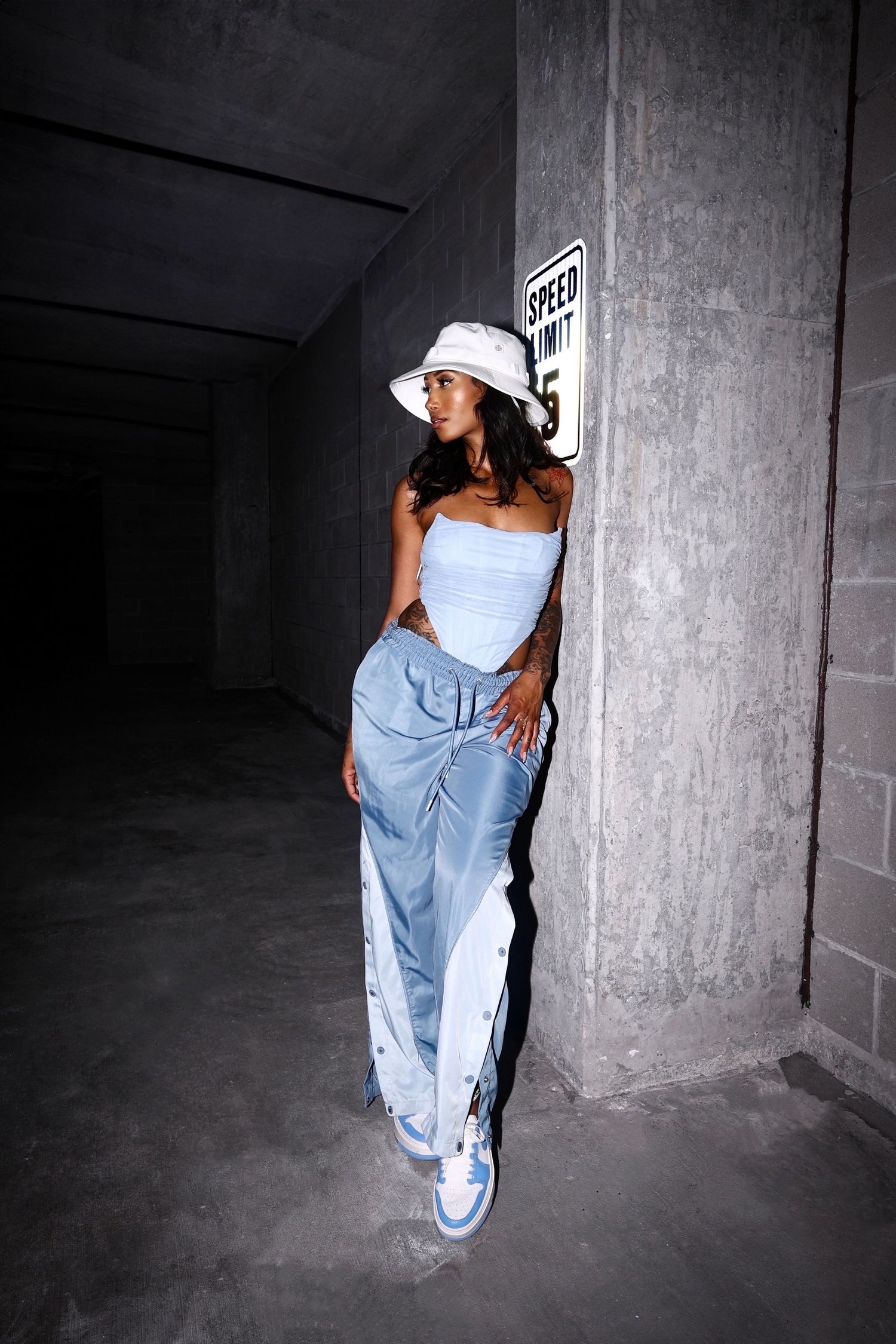 Fashion model in white top and denim posing against concrete wall in urban setting.