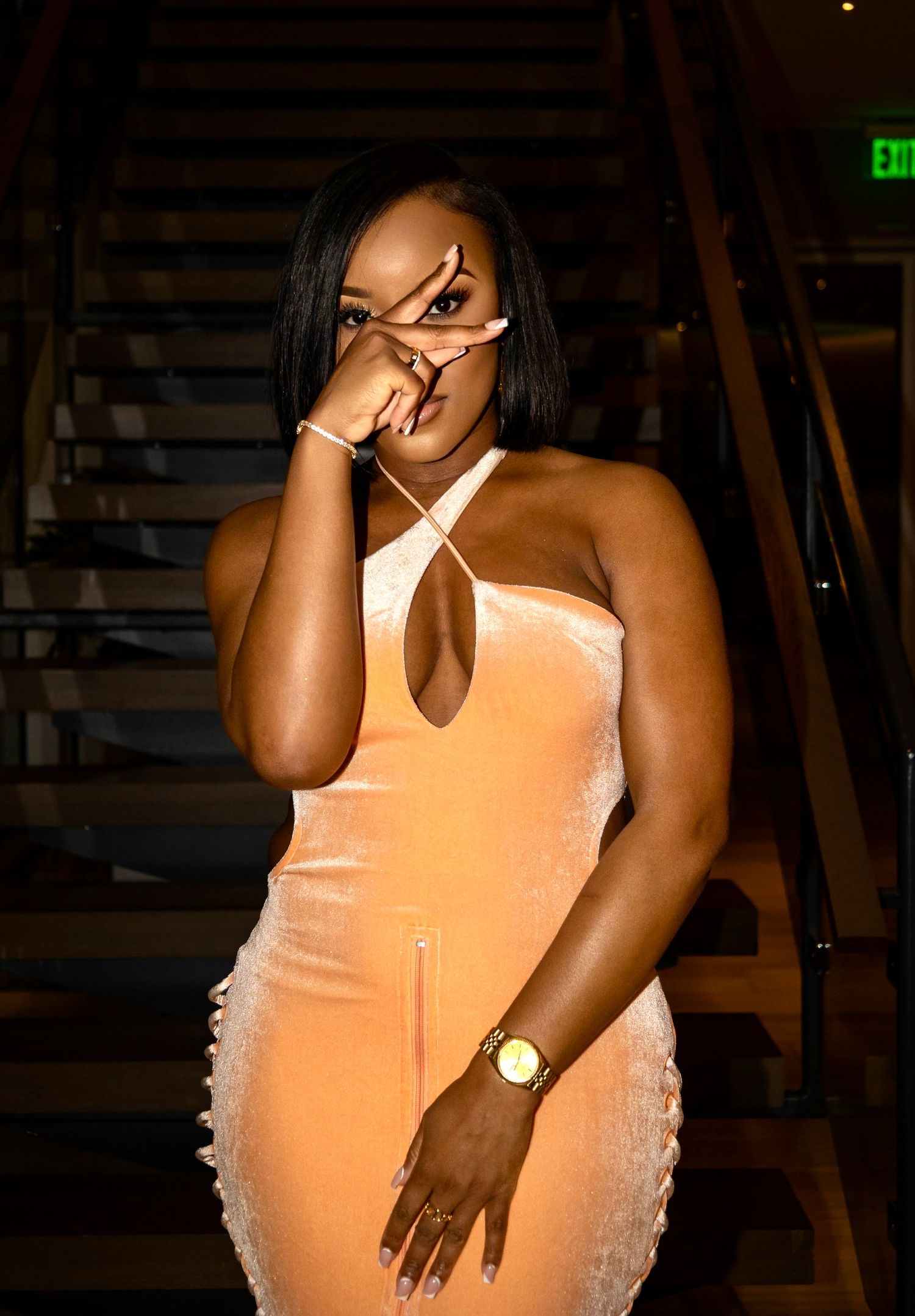 Model in peach bodycon dress poses on staircase.
