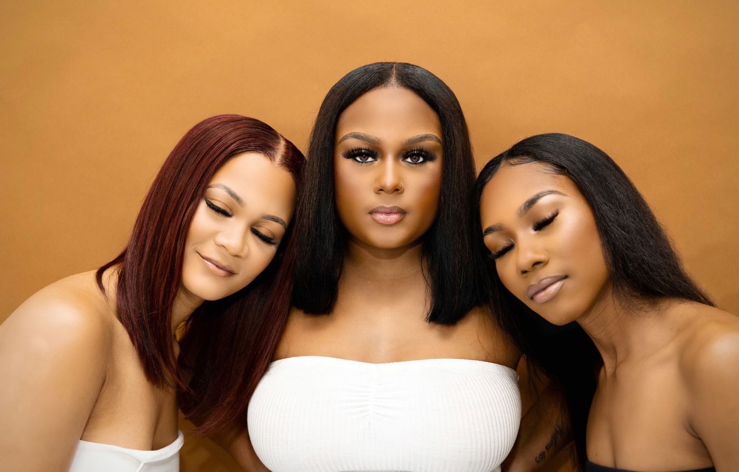Three models in white tops pose together against warm orange background.