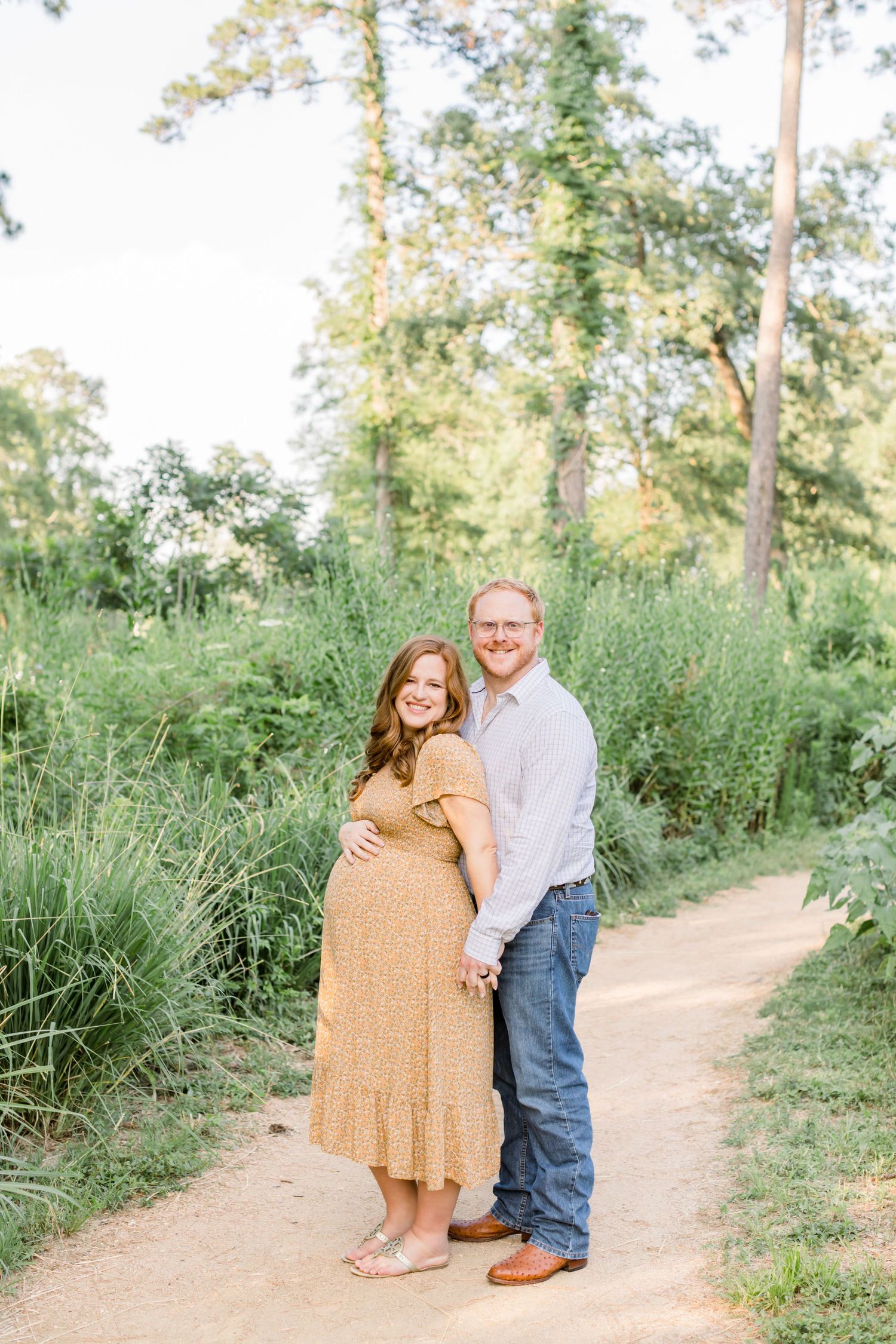 Couple poses together on dirt trail for maternity photos in natural setting.