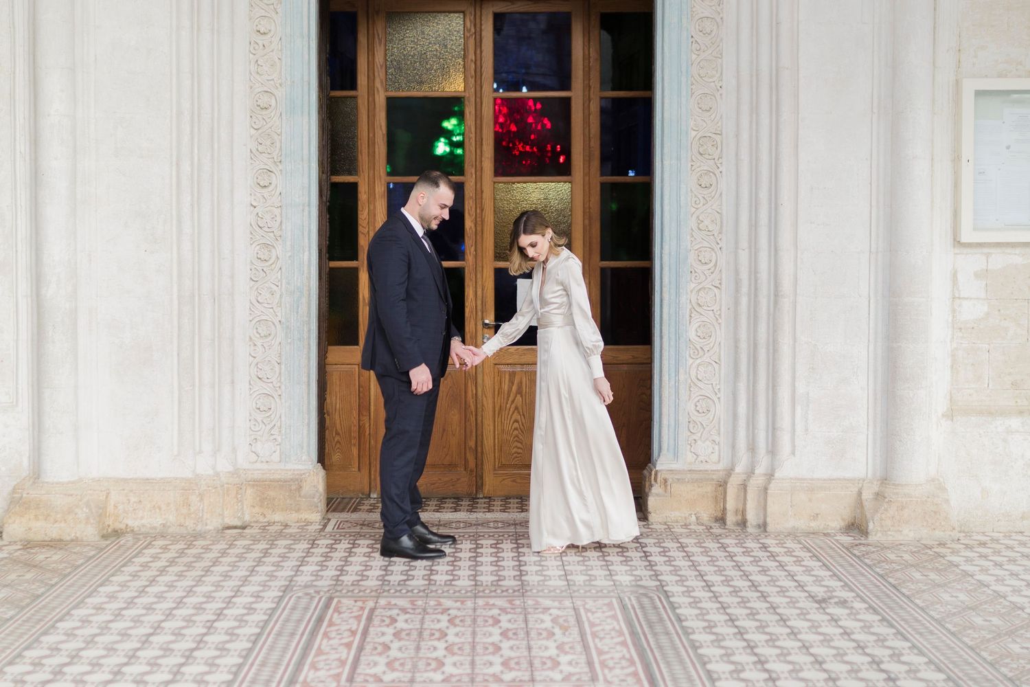 Bride and groom hold hands in front of ornate church doors.