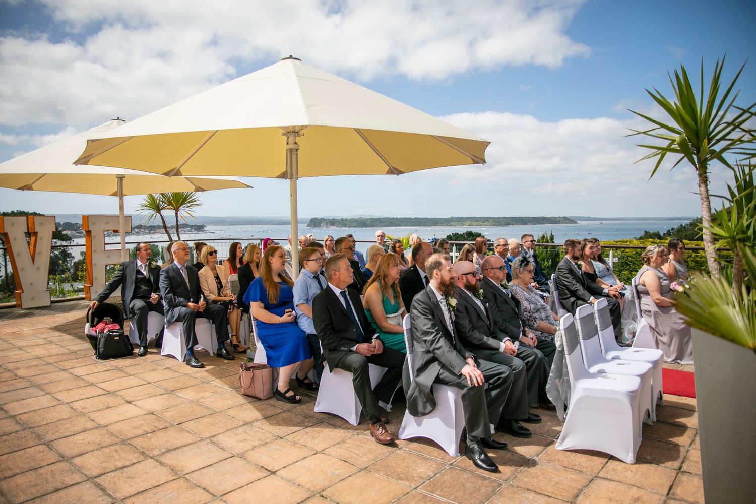 Outdoor wedding ceremony setup with white chairs and yellow umbrellas overlooking the ocean.