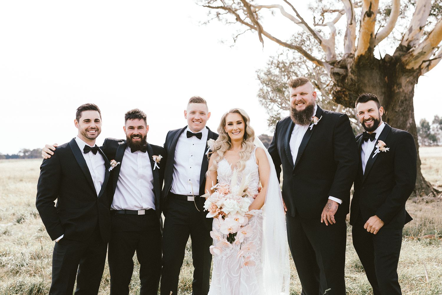 Elegant wedding party in formal attire gathered outdoors for a group portrait.