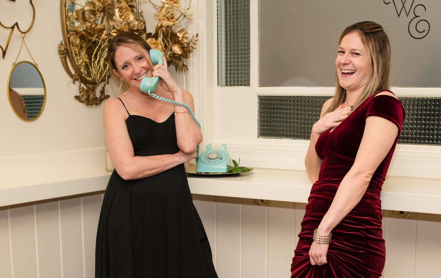 Wedding party members in burgundy dresses laughing together indoors.