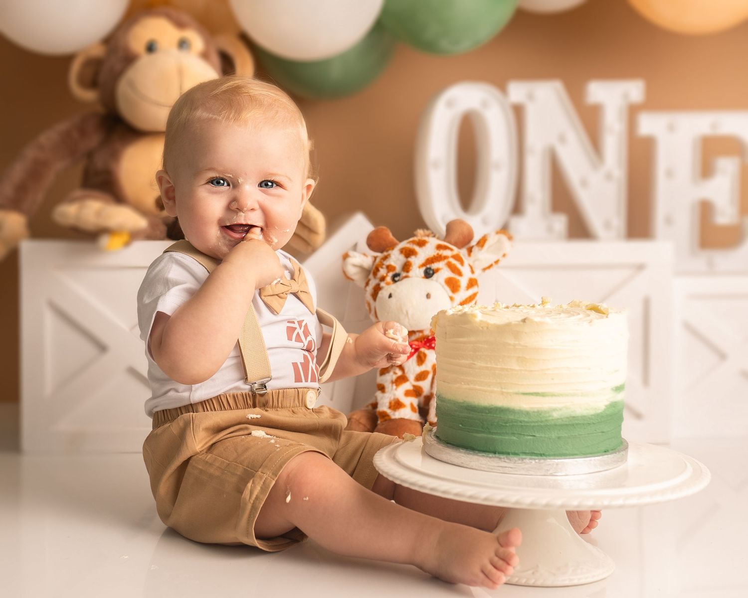 baby boy at his cake smash with finger in mouth and cake photographed by cake smash photographer swansea