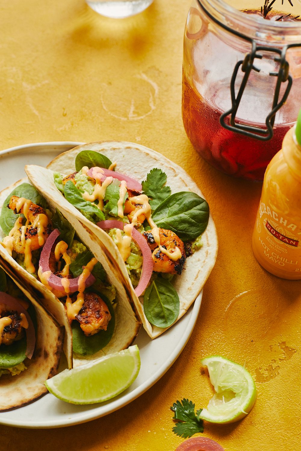 Shrimp tacos with pickled onions, lettuce, and lime served on a white plate with orange drink.