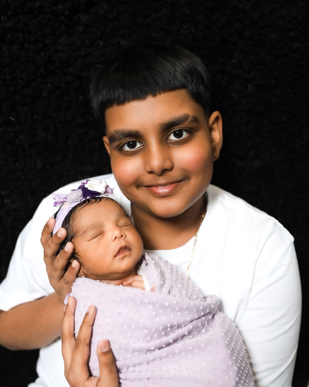 Close-up portrait of parent holding sleeping newborn baby swaddled in light purple wrap.