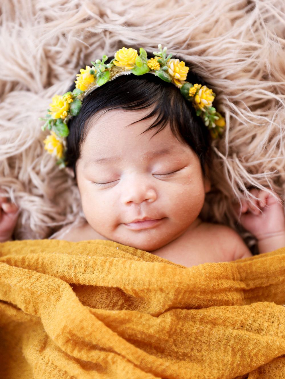 Sleeping baby wearing yellow flower crown on furry backdrop.
