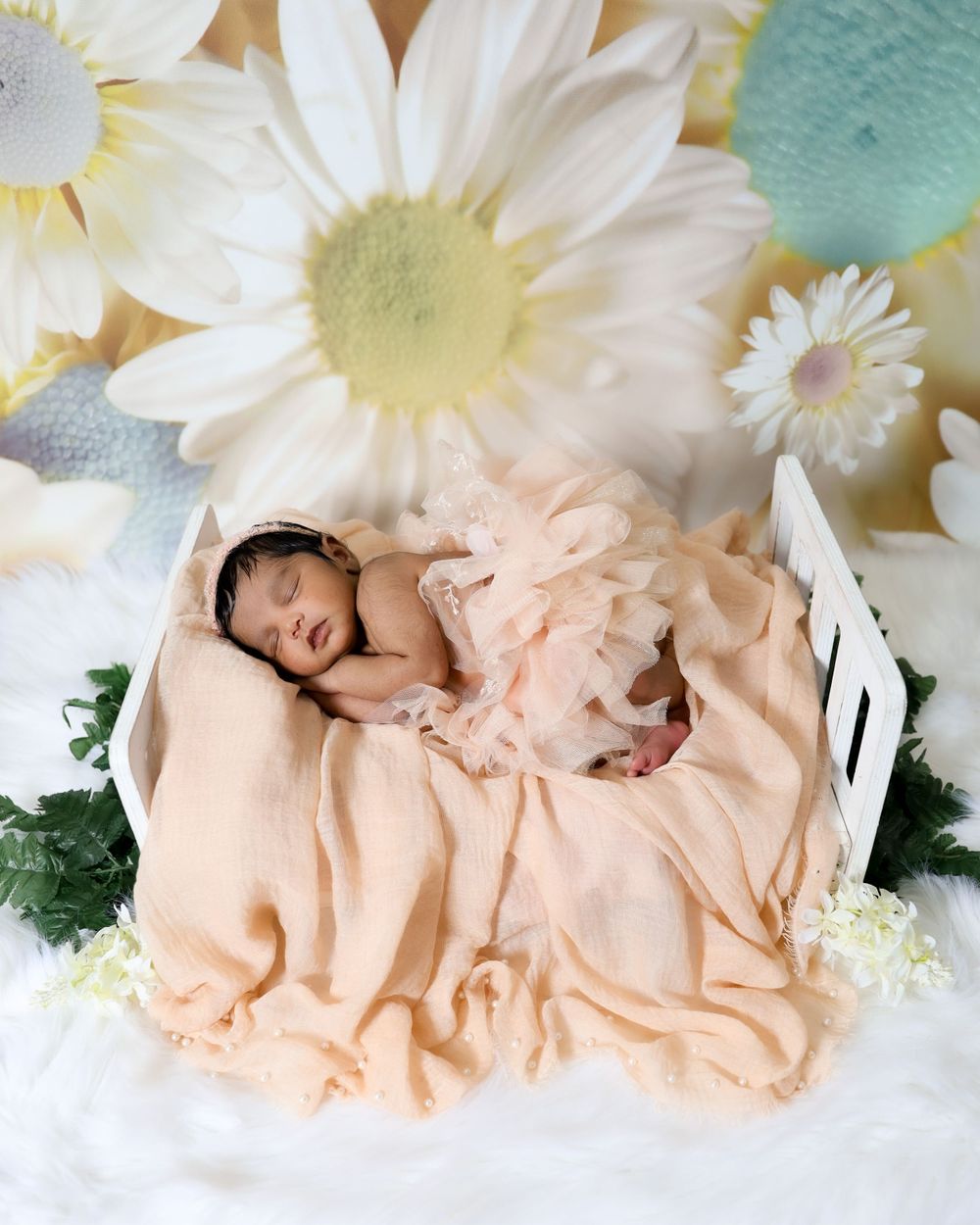 Newborn baby sleeping peacefully in peach dress surrounded by white daisy flowers.