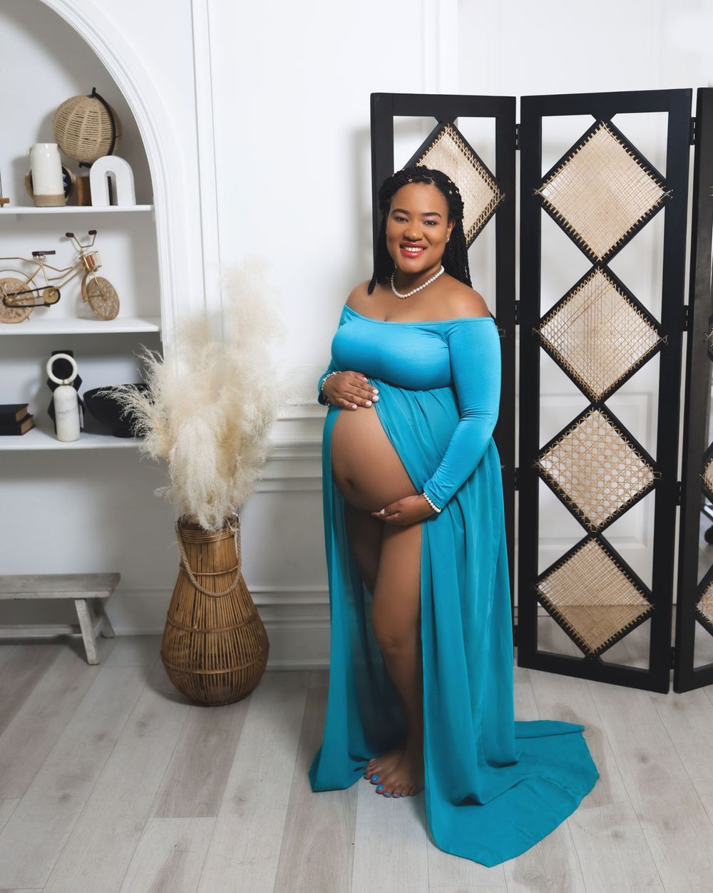 Maternity photo of woman in flowing turquoise dress posing in front of decorative screen.
