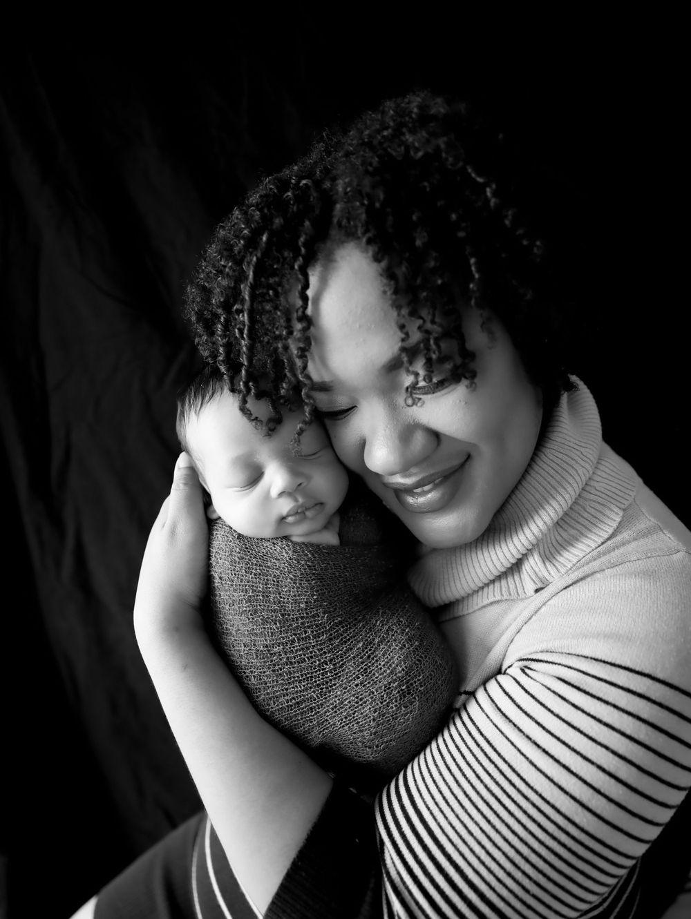Black and white portrait of parent holding sleeping newborn against dark background.
