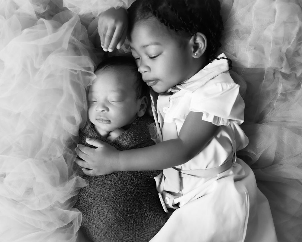 Black and white portrait of siblings sharing tender moment on soft tulle backdrop.