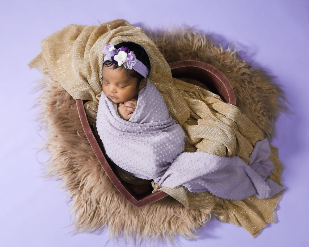 Sleeping newborn wrapped in gray swaddle on furry brown blanket with purple background.