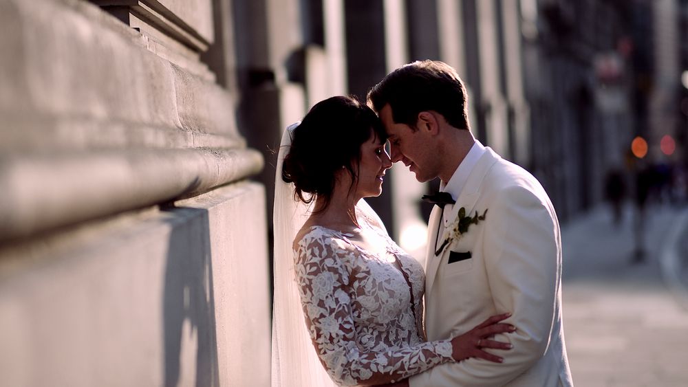 A romantic moment between newlyweds against a textured stone wall in soft lighting.