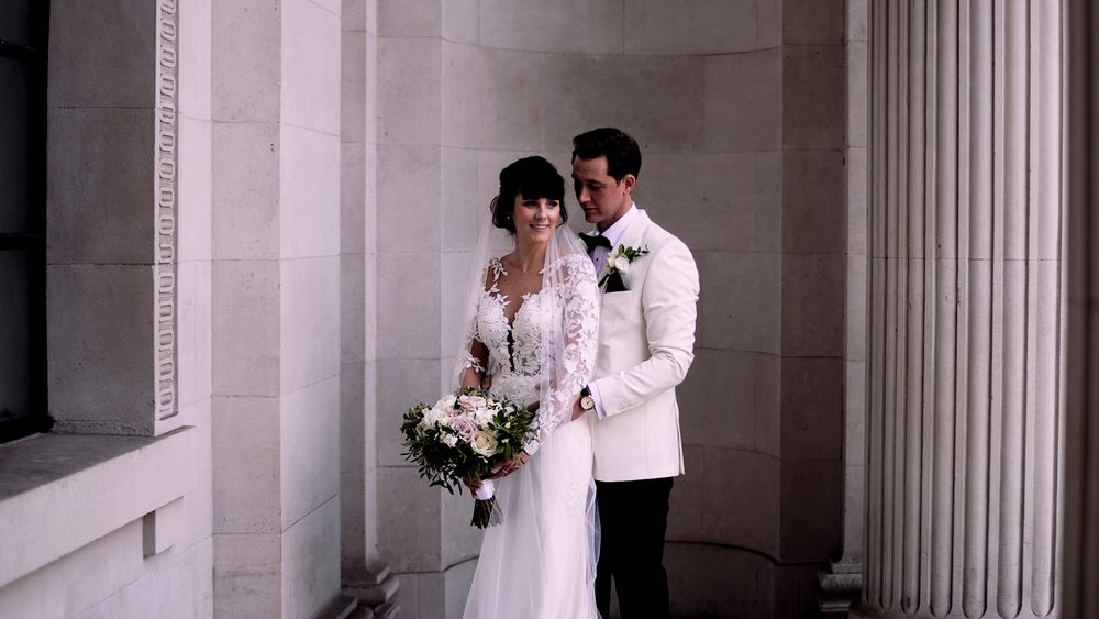 Elegant wedding couple poses in a classical architectural setting with white columns.