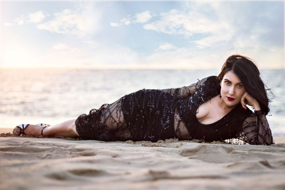 Woman at Point Peron Rockingham beach in a beaded dress, laying on her side propping her head up with her hand.