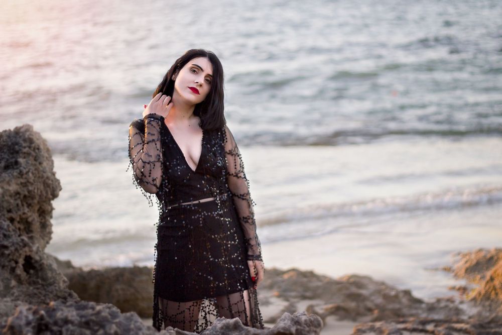 Woman with dark shoulder length hair wearing black evening dress standing on beach at Point Peron Rockingham.