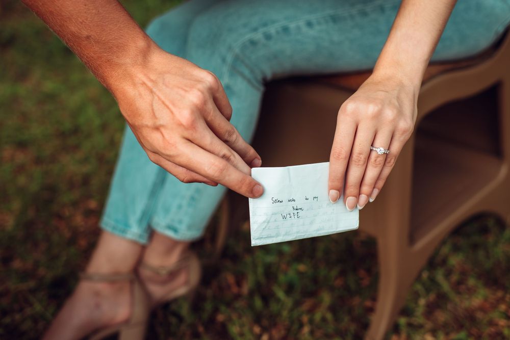 Hands exchanging a handwritten note on a wooden chair outdoors.