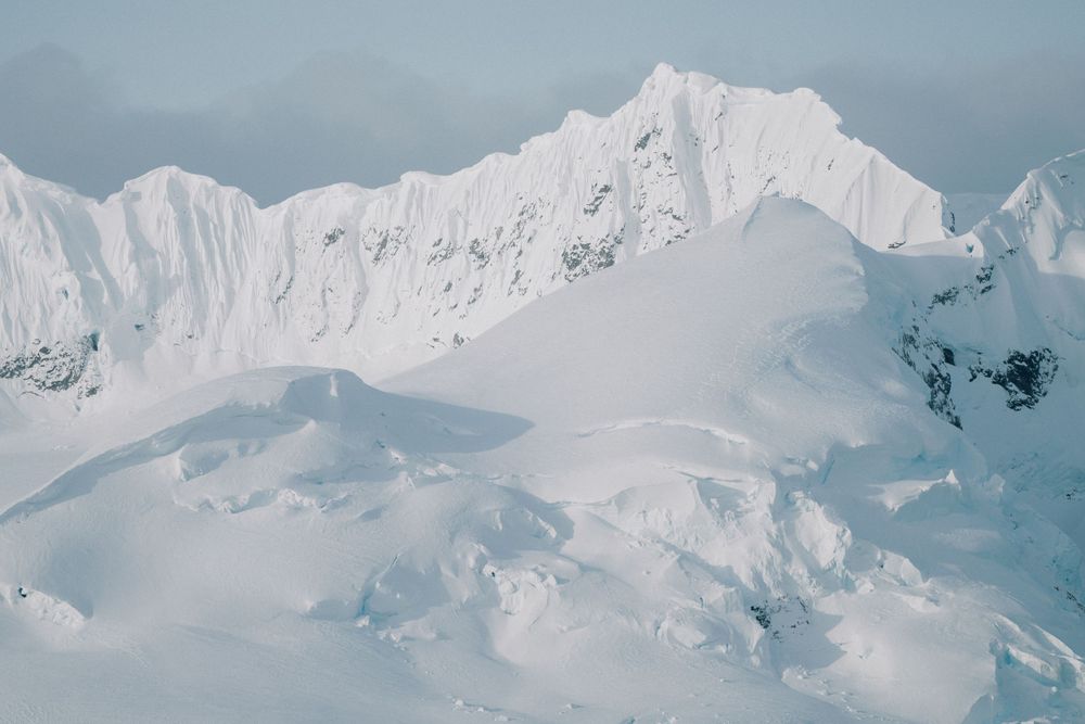 Snow-covered mountain peaks rise dramatically against a bright sky in a pristine winter landscape.