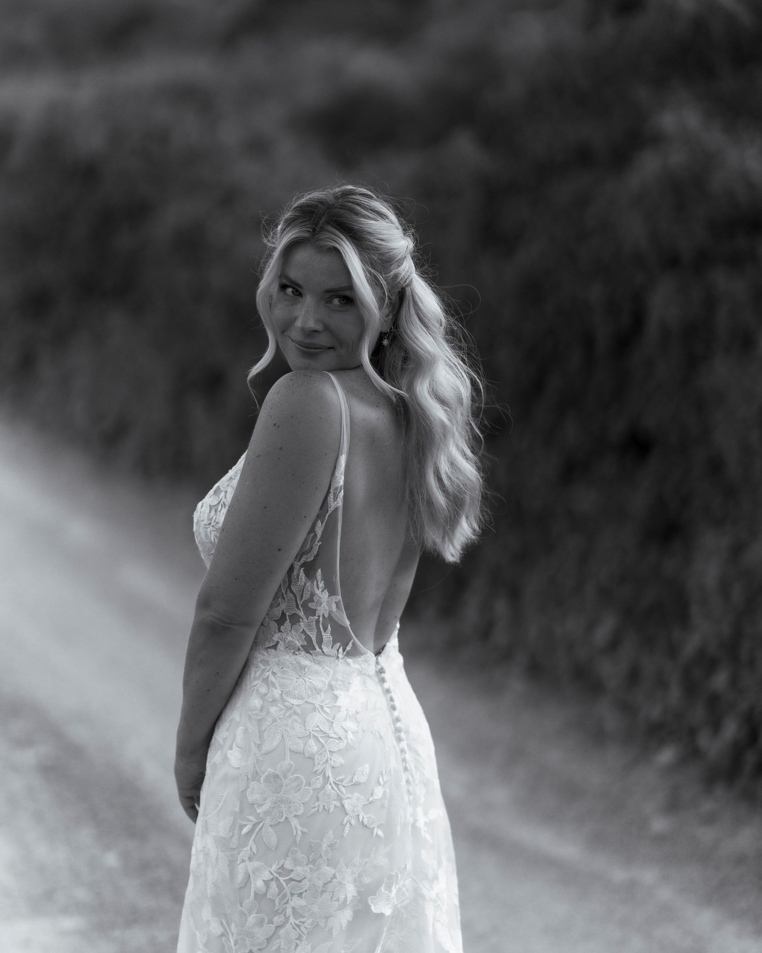 Black and white photo of the a bride looking over her shoulder, showing her beautiful backless wedding dress.