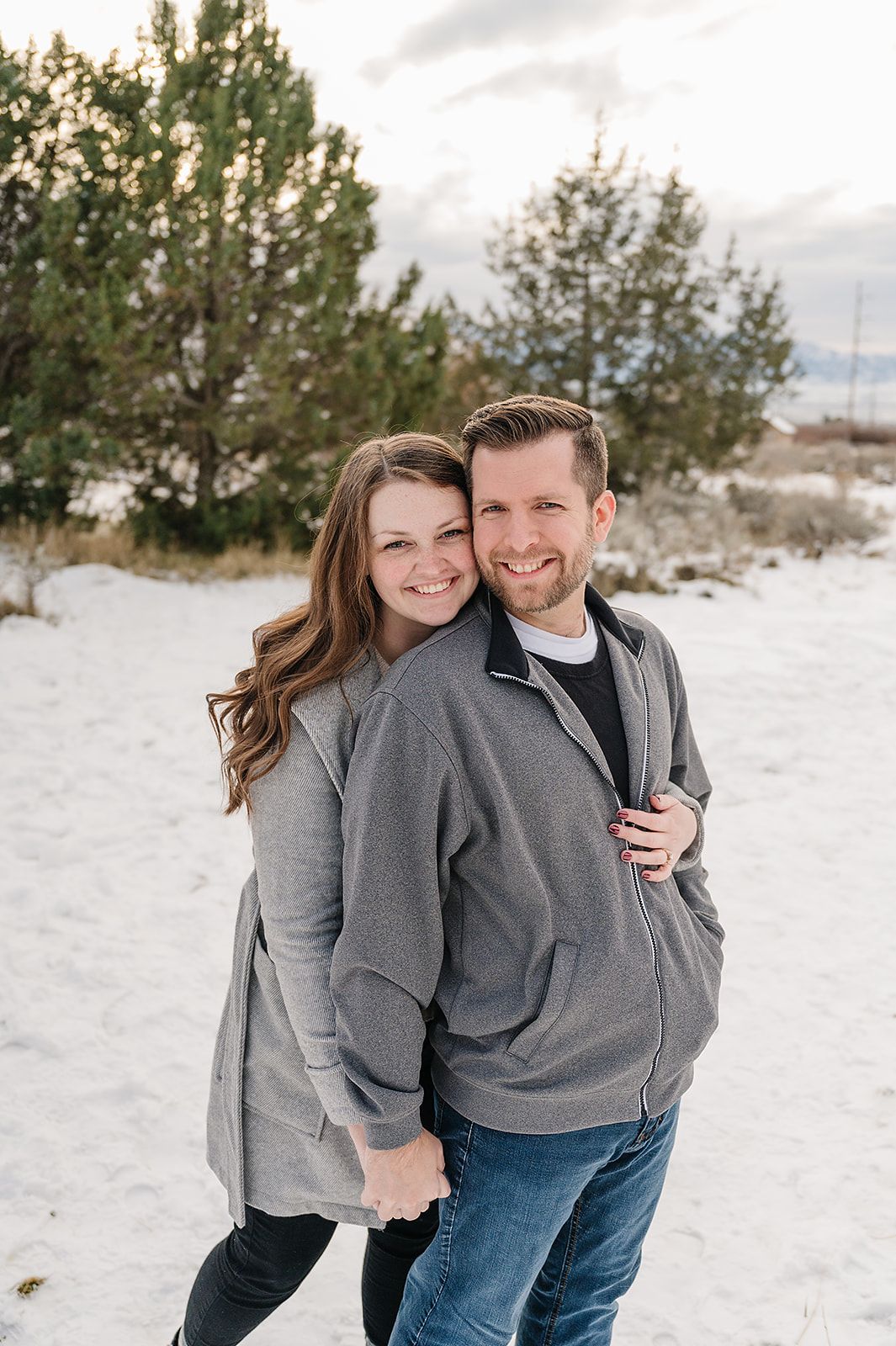 A casual winter portrait in matching grey sweaters with snow and evergreens.