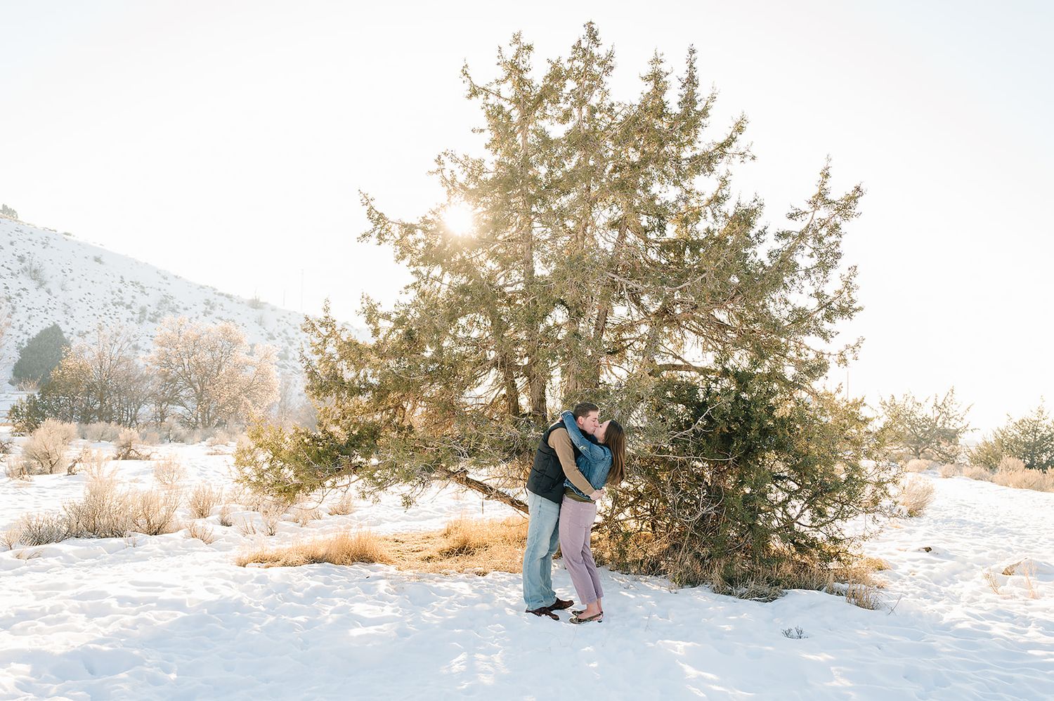 Couple sharing a romantic moment in fresh snow with sunlit pine trees.