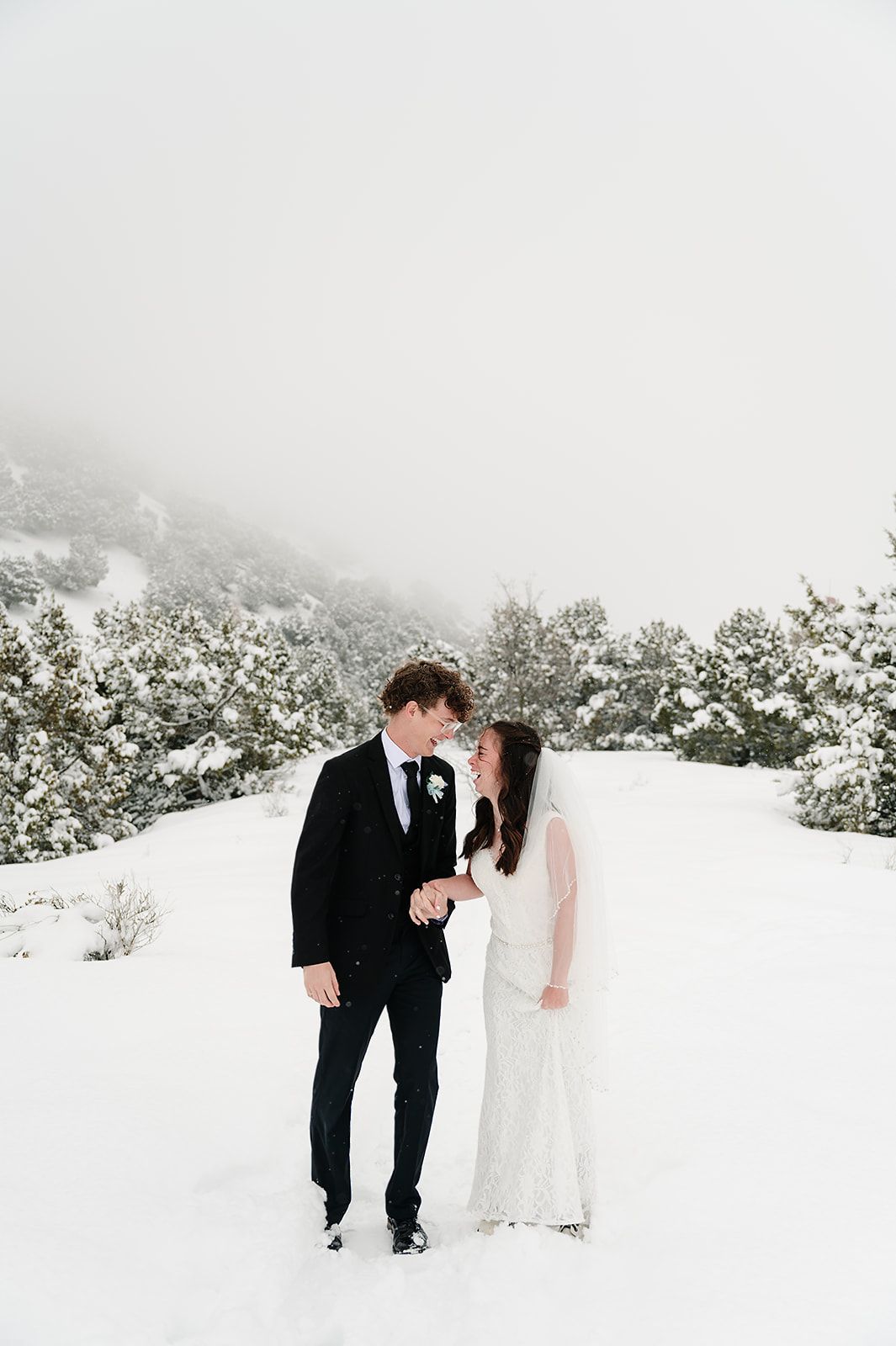 Couple in formal attire share intimate moment in snowy mountain landscape.
