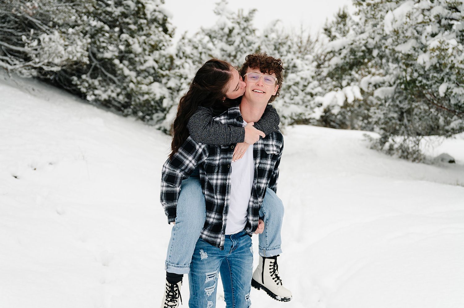 Couple in casual winter wear enjoying snowy day among evergreen trees.