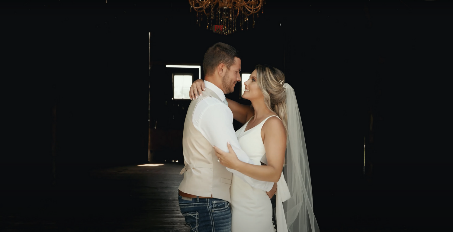 Intimate wedding moment captured against dark background with dramatic lighting.