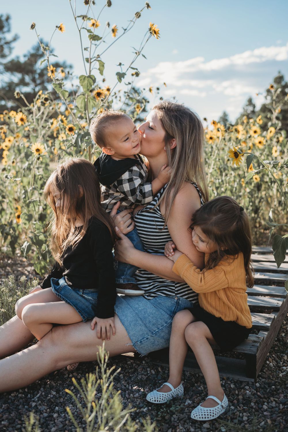 Family sharing tender moment together on wooden platform among sunflowers.
